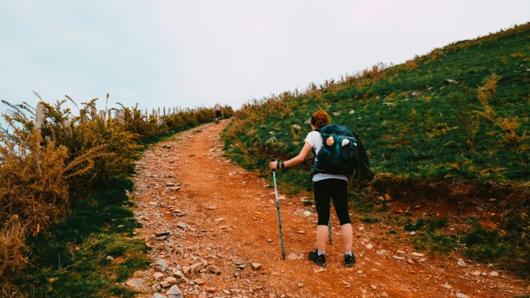 A person hiking uphill with a light daypack, symbolizing hiking and weight loss benefits.