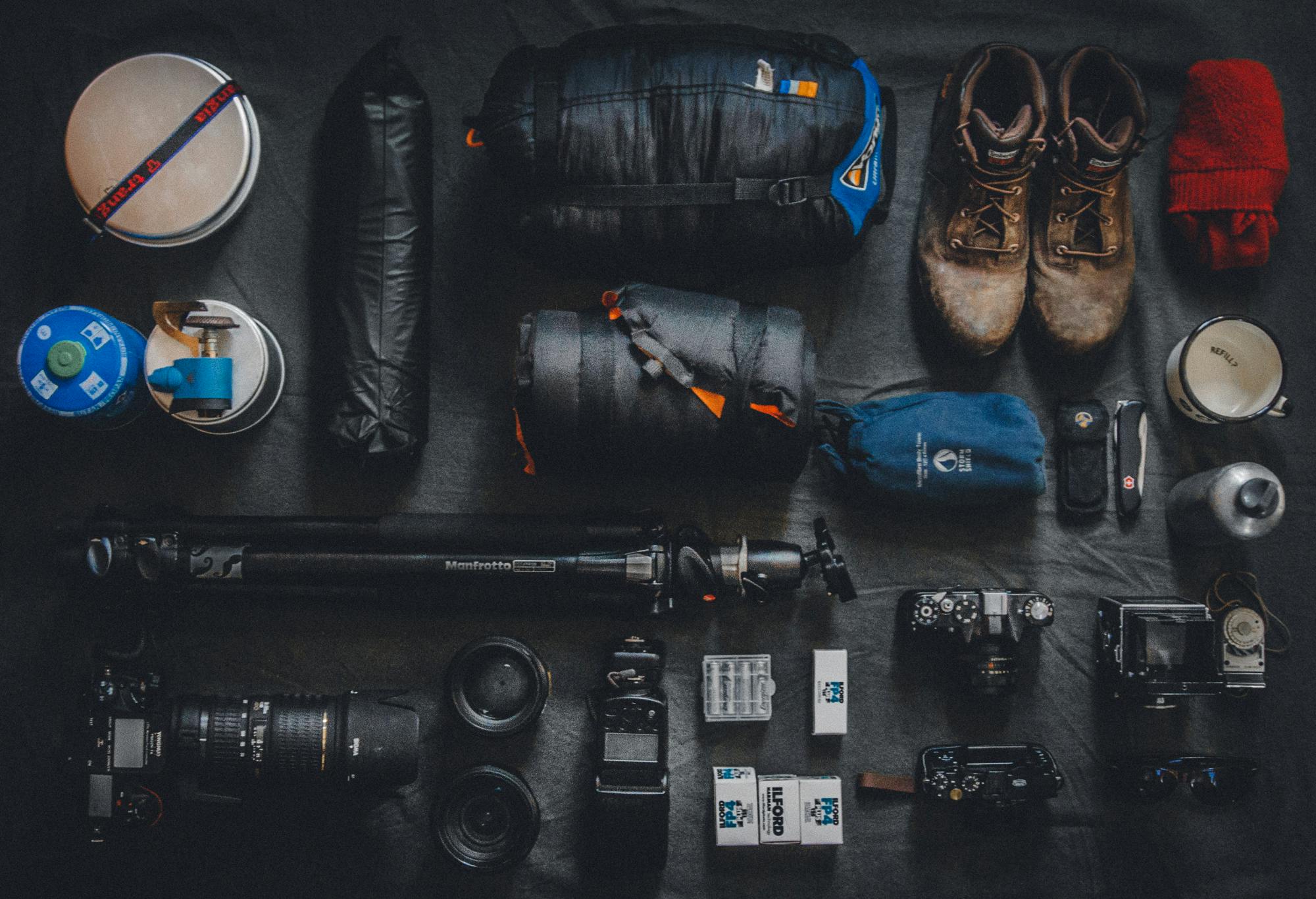 A flat lay of beginner hiking gear essentials including boots, backpack, map, and safety items on a wooden surface