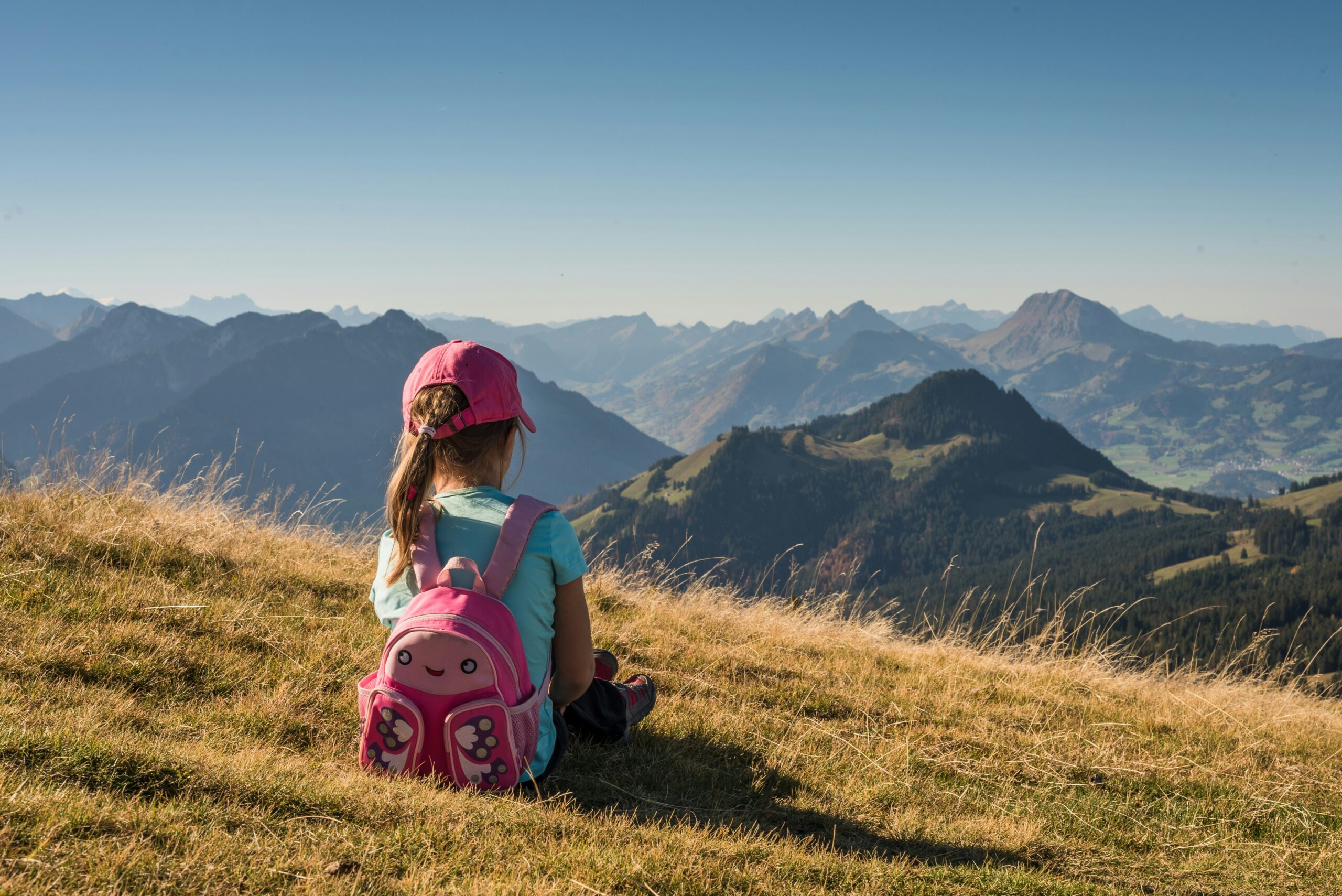 Child sitting on a mountain trail with backpack — introduce hiking to kids at an early age