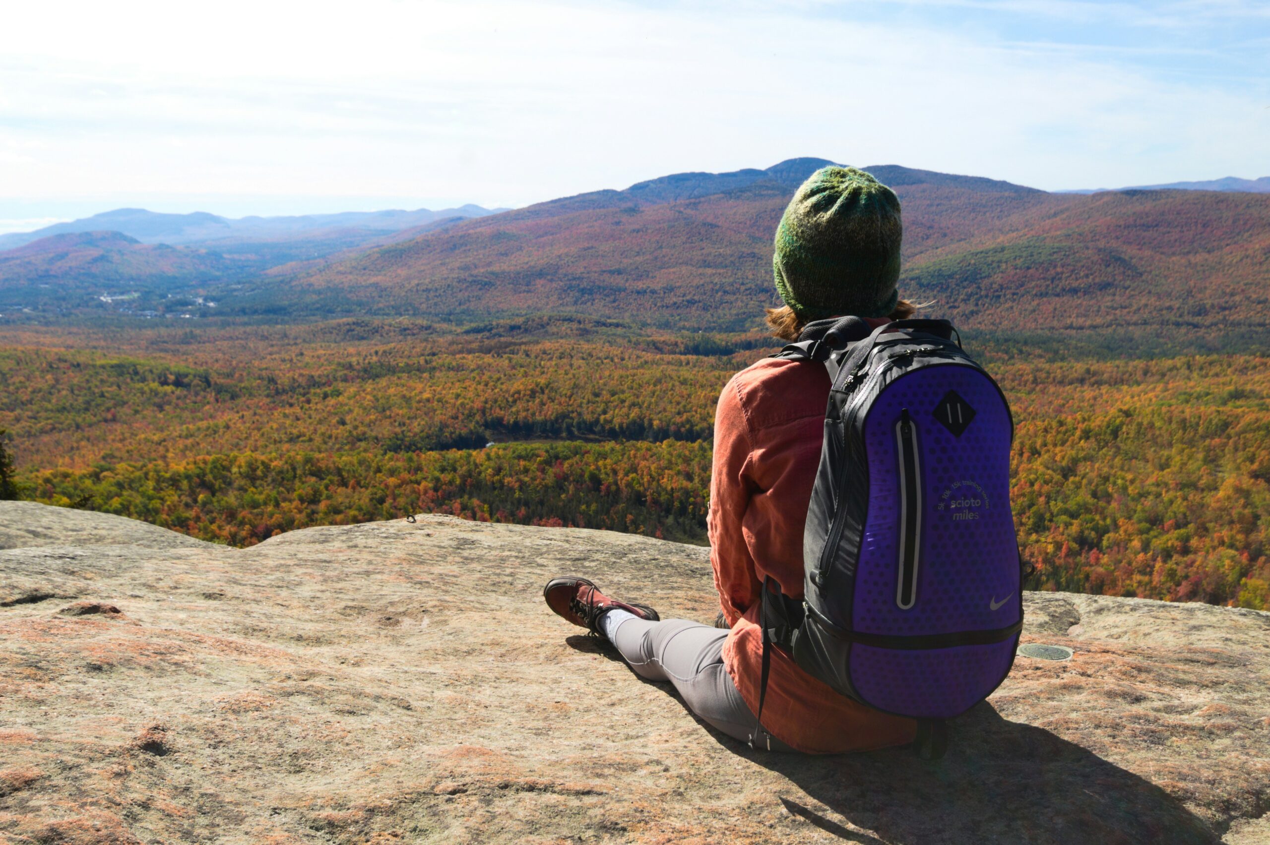 Beginner hiker enjoying one of the best hikes in fall while sitting on a rocky overlook with autumn foliage view